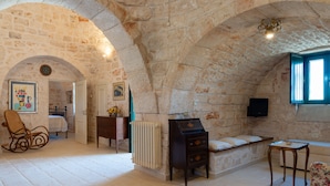 A stone-walled room with a fireplace, a wooden dresser, a rocking chair, and a small table. - Stile e relax nei trulli by Wonderful Italy (Martina Franca)