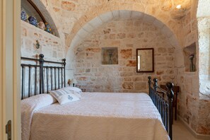 A bedroom with a stone wall, a bed with a metal headboard, and a small window.
