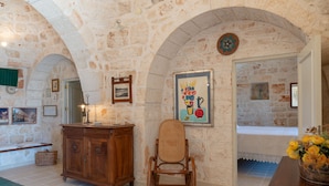 A room with stone walls, a wooden cabinet, a wicker chair, and a vase with flowers. - Stile e relax nei trulli by Wonderful Italy (Martina Franca)