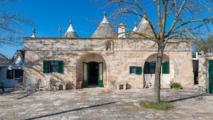 A stone building with arched doorways and green shutters, a courtyard with stone flooring, and a tree in the foreground. - Stile e relax nei trulli by Wonderful Italy (Martina Franca)