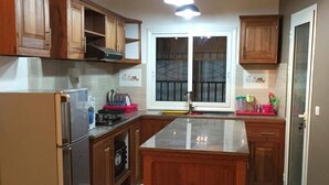 A kitchen with wooden cabinets, a stainless steel refrigerator, a central island, and pendant lighting. - RESIDENCE BAOBAB LOFT (Morondava)