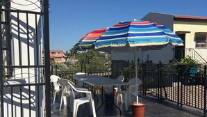 An outdoor patio area with a table and chairs, striped umbrellas, and a tiled floor. - RESIDENCE BAOBAB LOFT (Morondava)