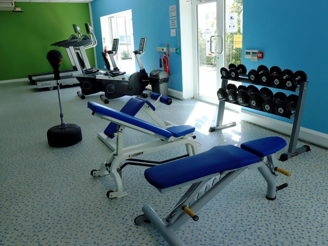 Uma academia com equipamentos de ginástica, incluindo um banco, halteres e esteira.