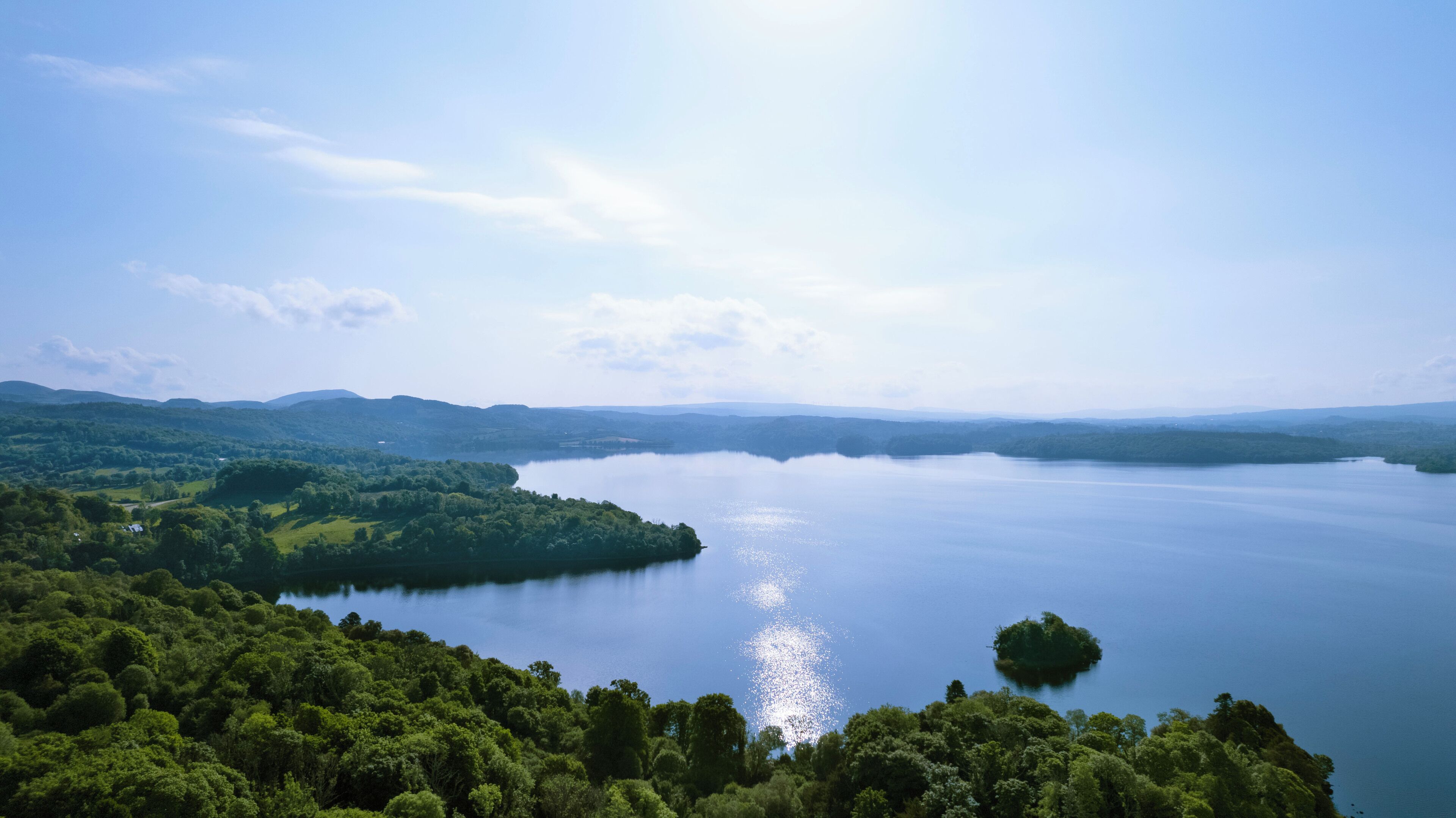 A lake surrounded by lush greenery and distant hills.
