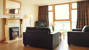 A living room with a fireplace, a sofa, a television, and large windows with curtains.