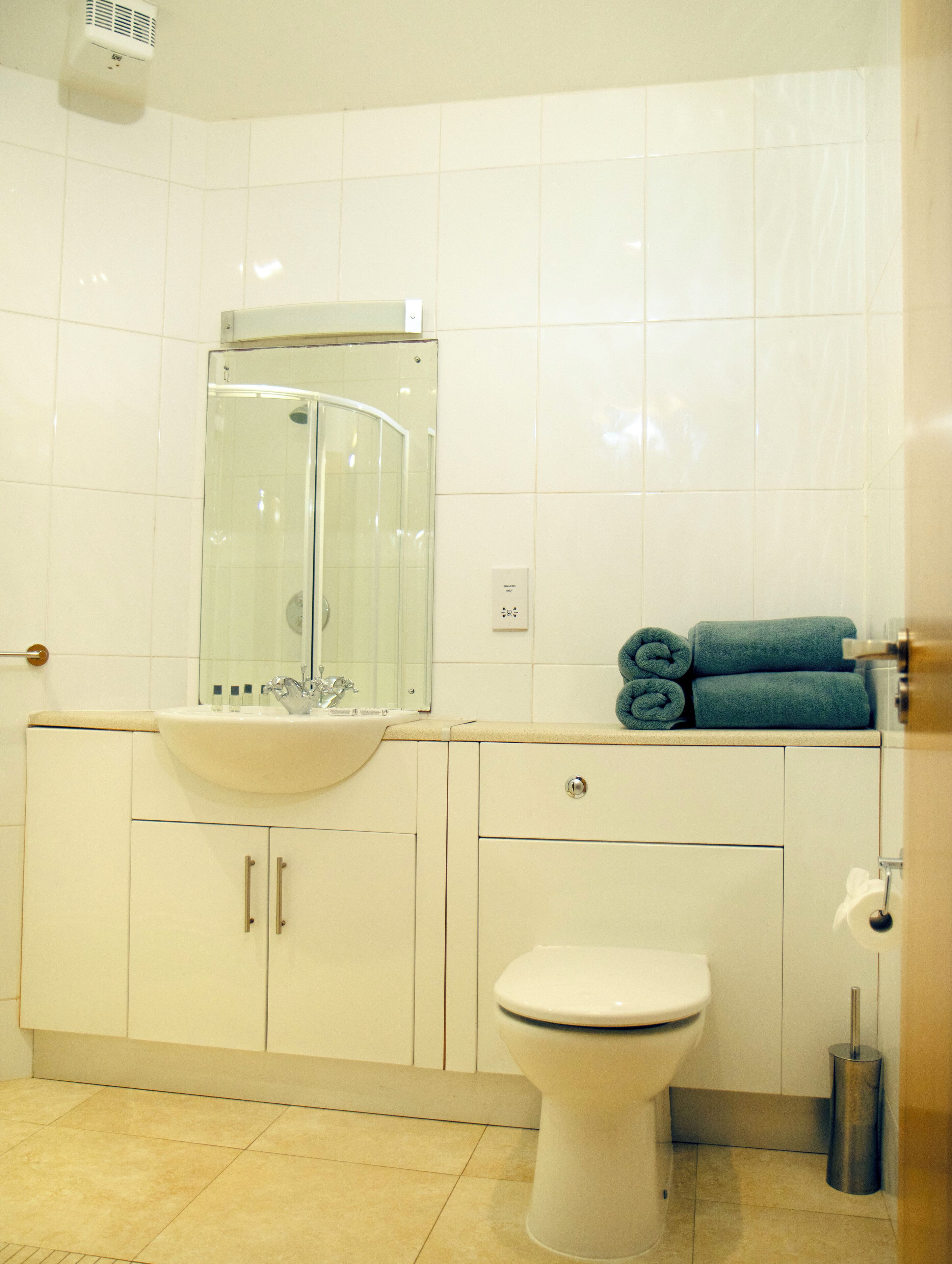 A bathroom with a white sink, a glass shower enclosure, a toilet, and a towel rack with towels.