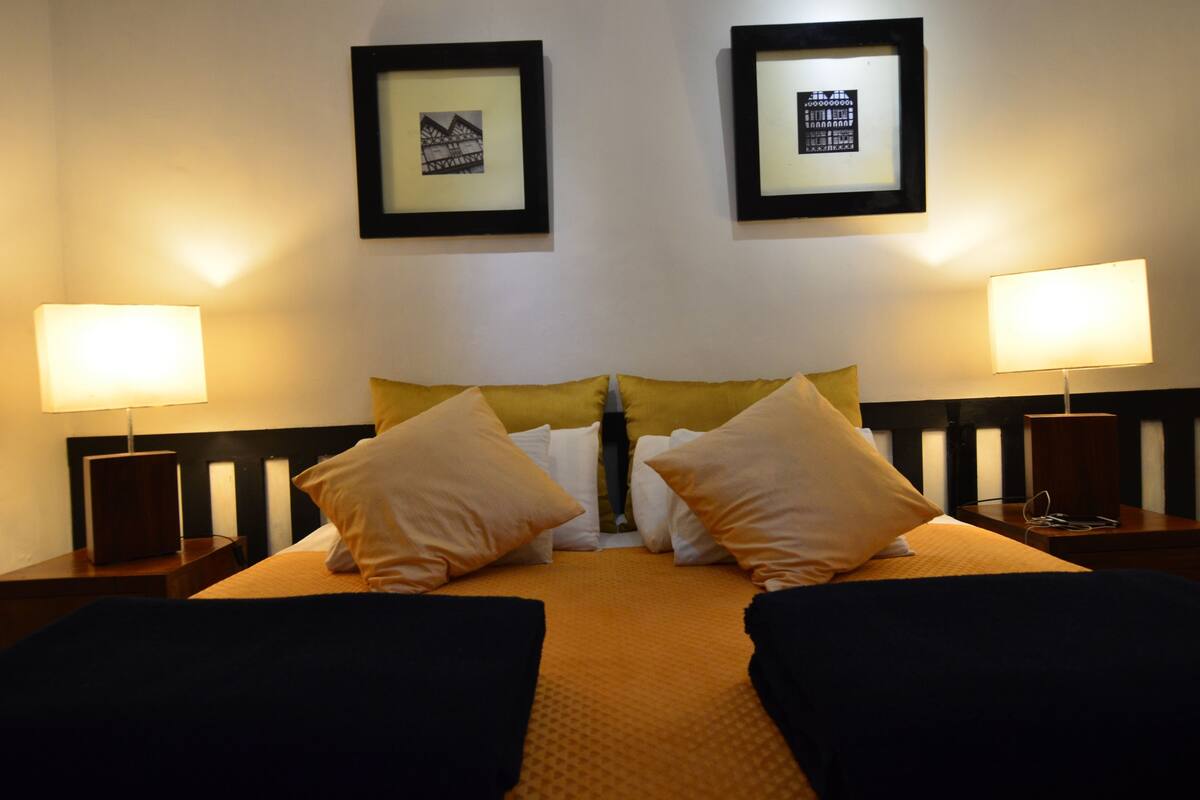 A hotel room with a bed, two nightstands, two lamps, and two framed pictures on the wall.