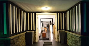 Ein Flur mit Streifenwänden, einer Steinwand an der Seite und einer hölzernen Bank. Am Ende des Flurs befindet sich eine Tür.