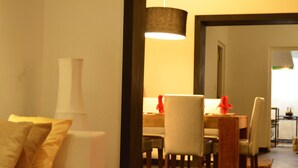 Een eetgedeelte met een tafel, stoelen, een hanglamp en een bank met kussens.