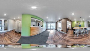 A modern reception area with a curved desk, a waiting area with a high chair, and a dining area with a large table and chairs. - WoodSpring Suites Davenport FL (Davenport)
