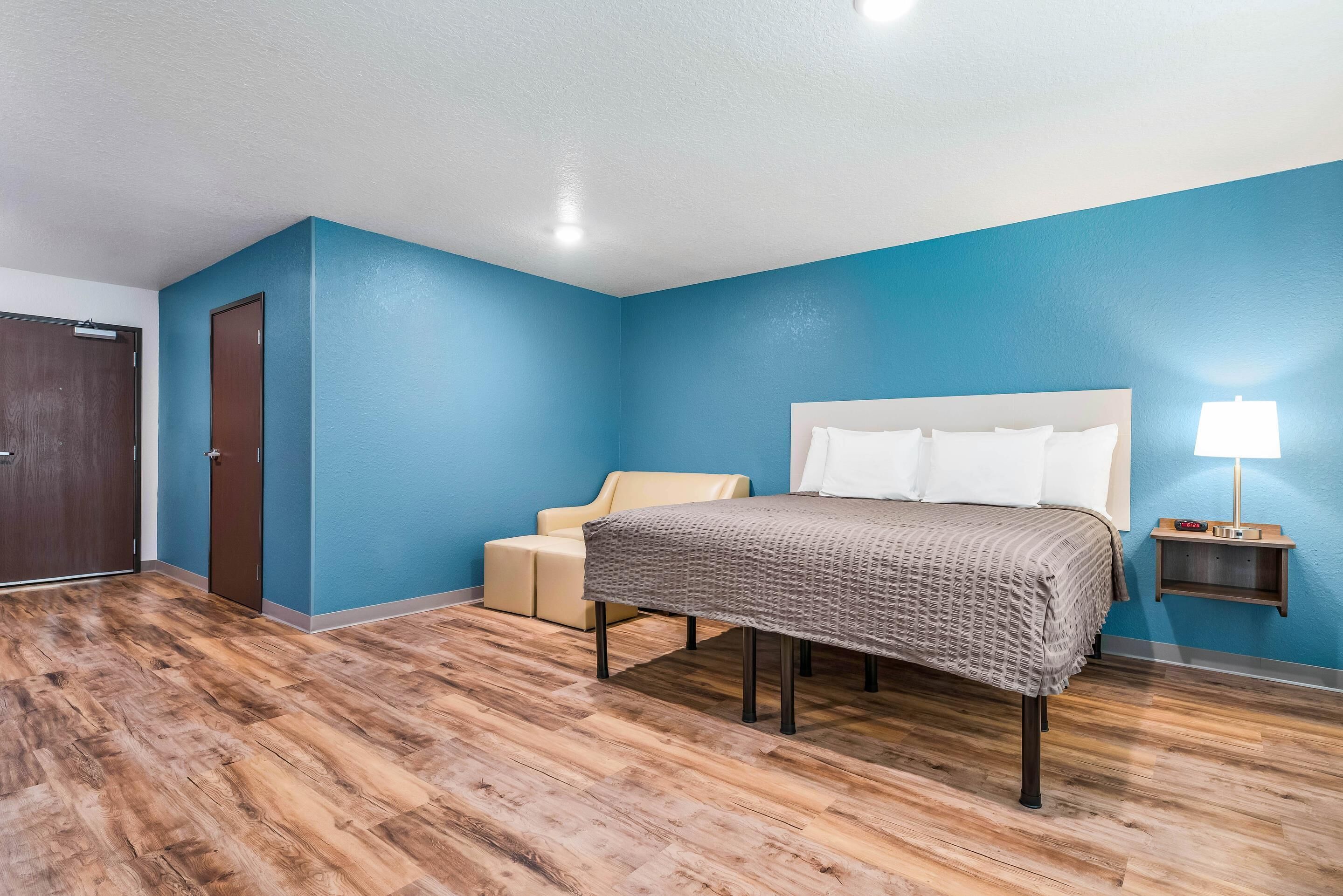 Un dormitorio con cama, mesita de noche, lámpara, puerta y una silla.