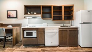 A compact kitchen with wooden cabinets, a microwave, a dishwasher, and a refrigerator. - WoodSpring Suites Davenport FL (Davenport)