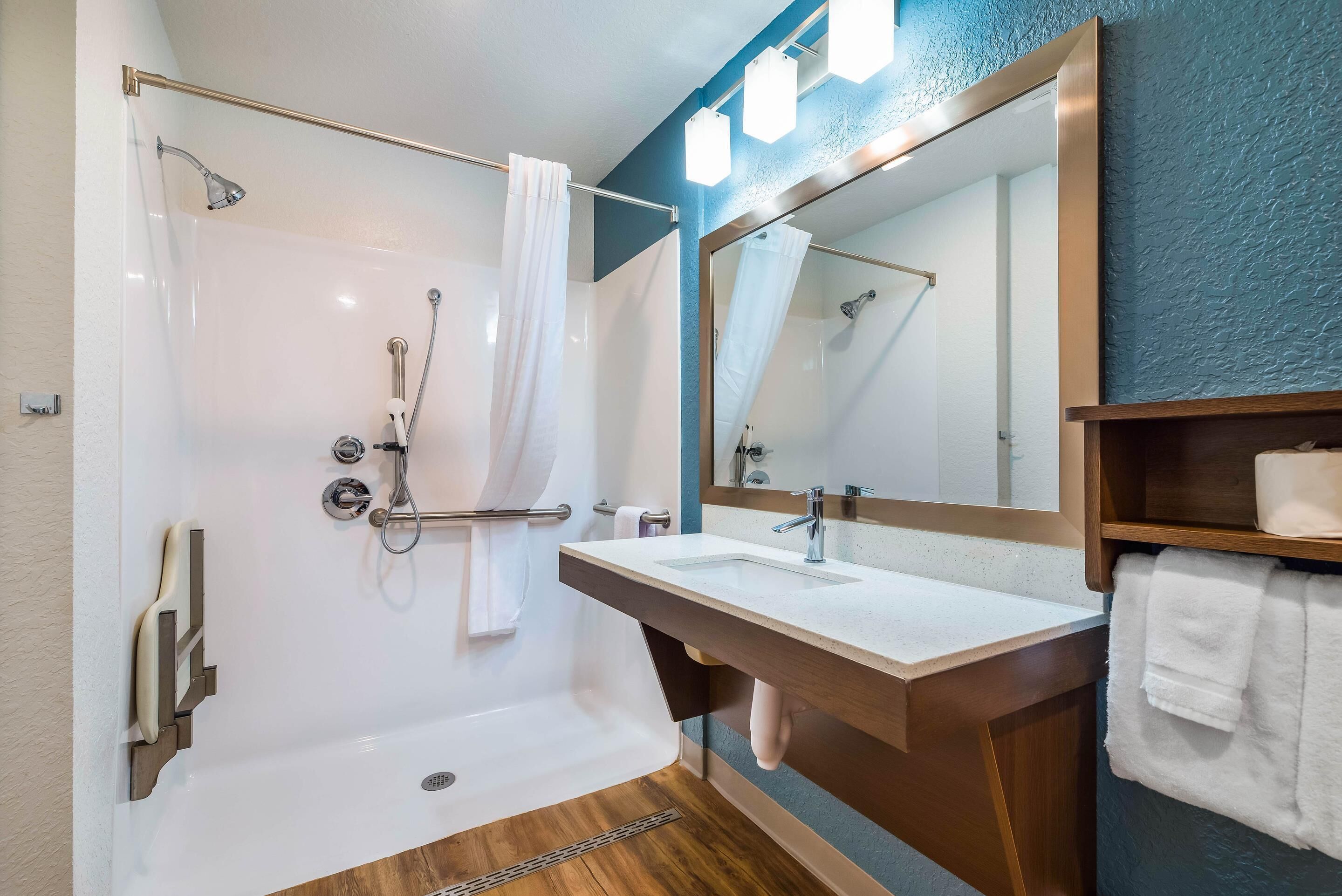 A modern bathroom with a glass-enclosed shower, a wooden vanity with a sink, and a large mirror.