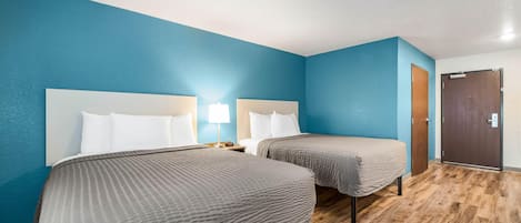 A hotel room with two beds, a wooden floor, and a blue wall.