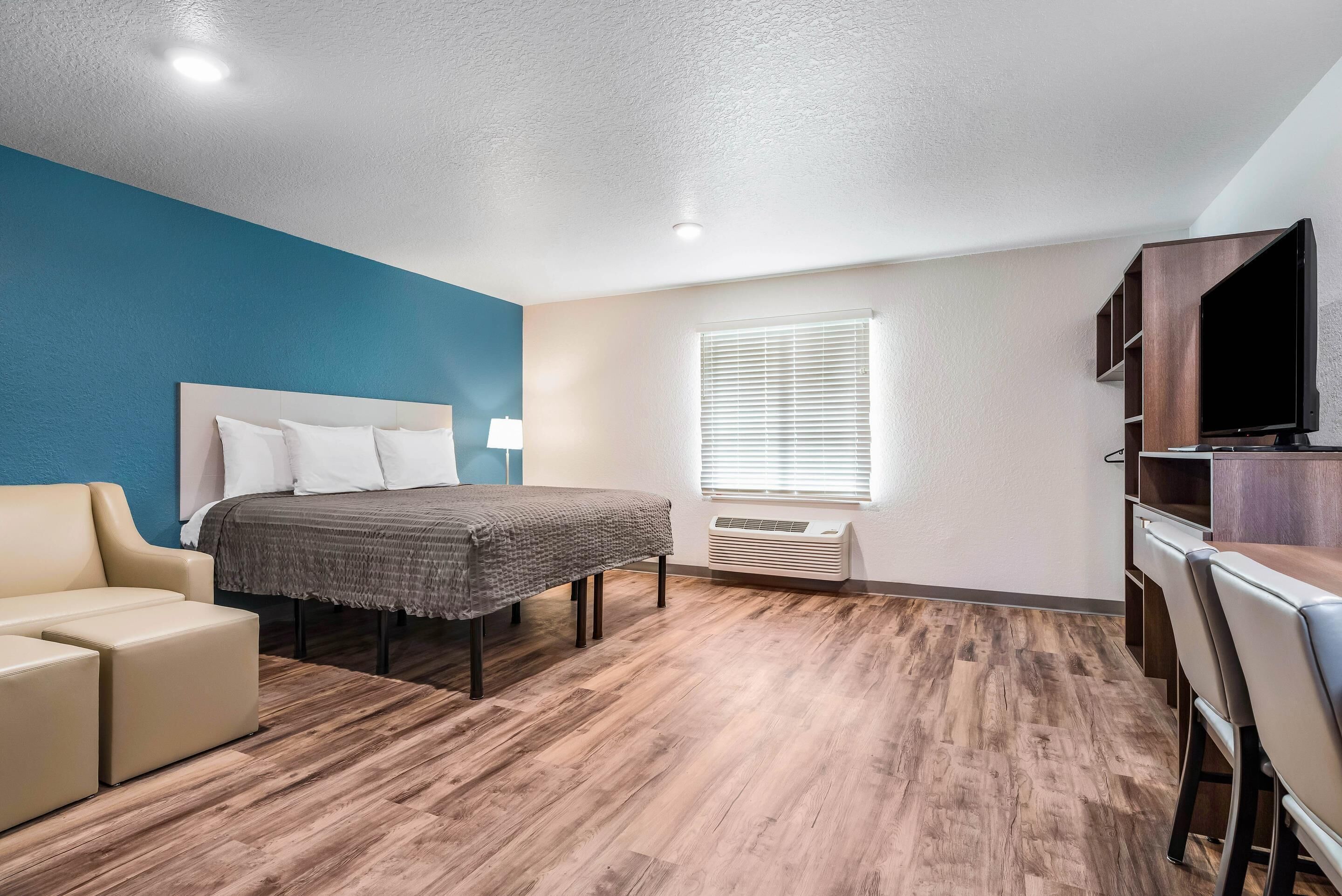 A hotel room with a bed, a sofa, a TV, and a window with blinds.