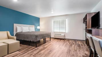 A hotel room with a bed, a sofa, a TV, and a window with blinds.