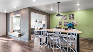 A modern dining area with a wooden table and white chairs, a green accent wall, and ceiling recessed lighting. - WoodSpring Suites Davenport FL (Davenport)