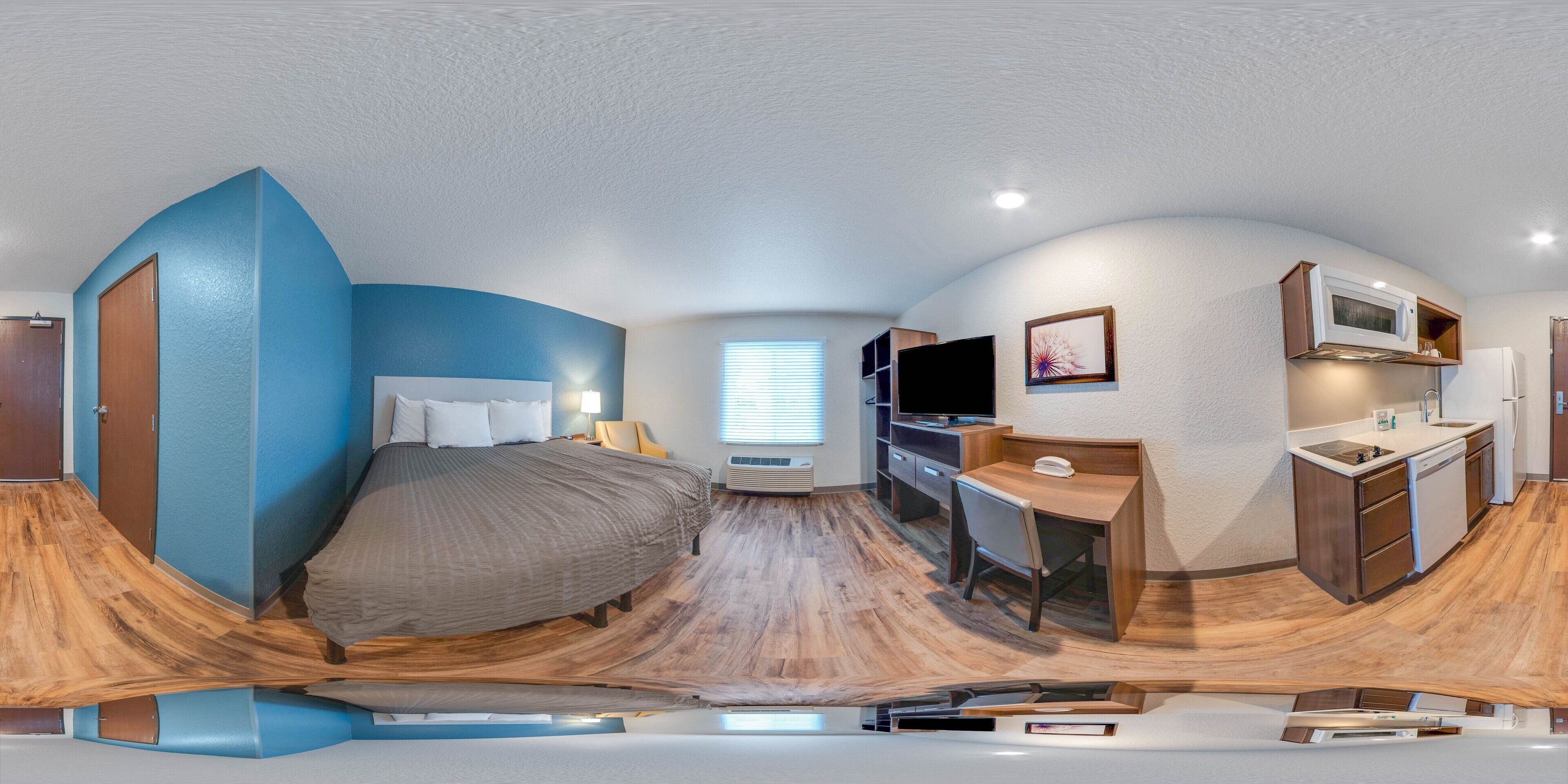 A compact room with a bed, a desk, a kitchenette, and a TV.