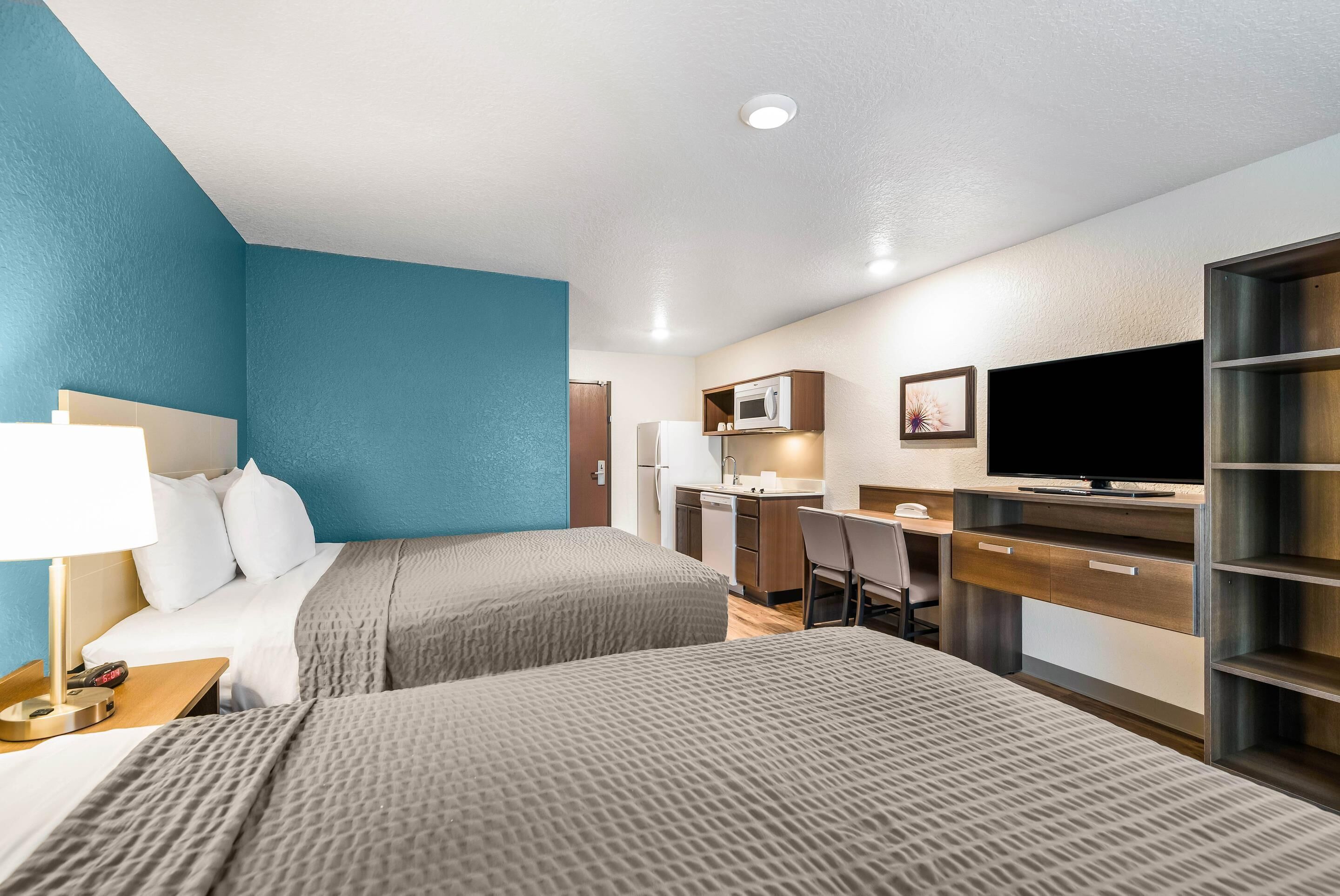 Habitación de hotel con cama, escritorio, televisor y kitchenette.