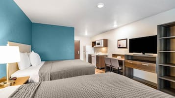 Habitación de hotel con cama, escritorio, televisor y kitchenette.
