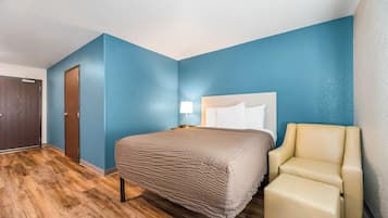 A hotel room with a bed, a chair, a nightstand, and a door.