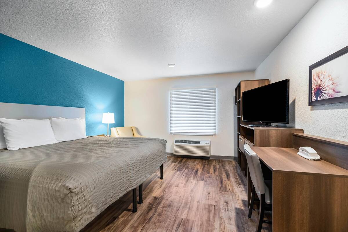 A hotel room with a bed, desk, TV, and air conditioning unit.