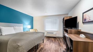 A hotel room with a bed, desk, TV, and air conditioning unit.