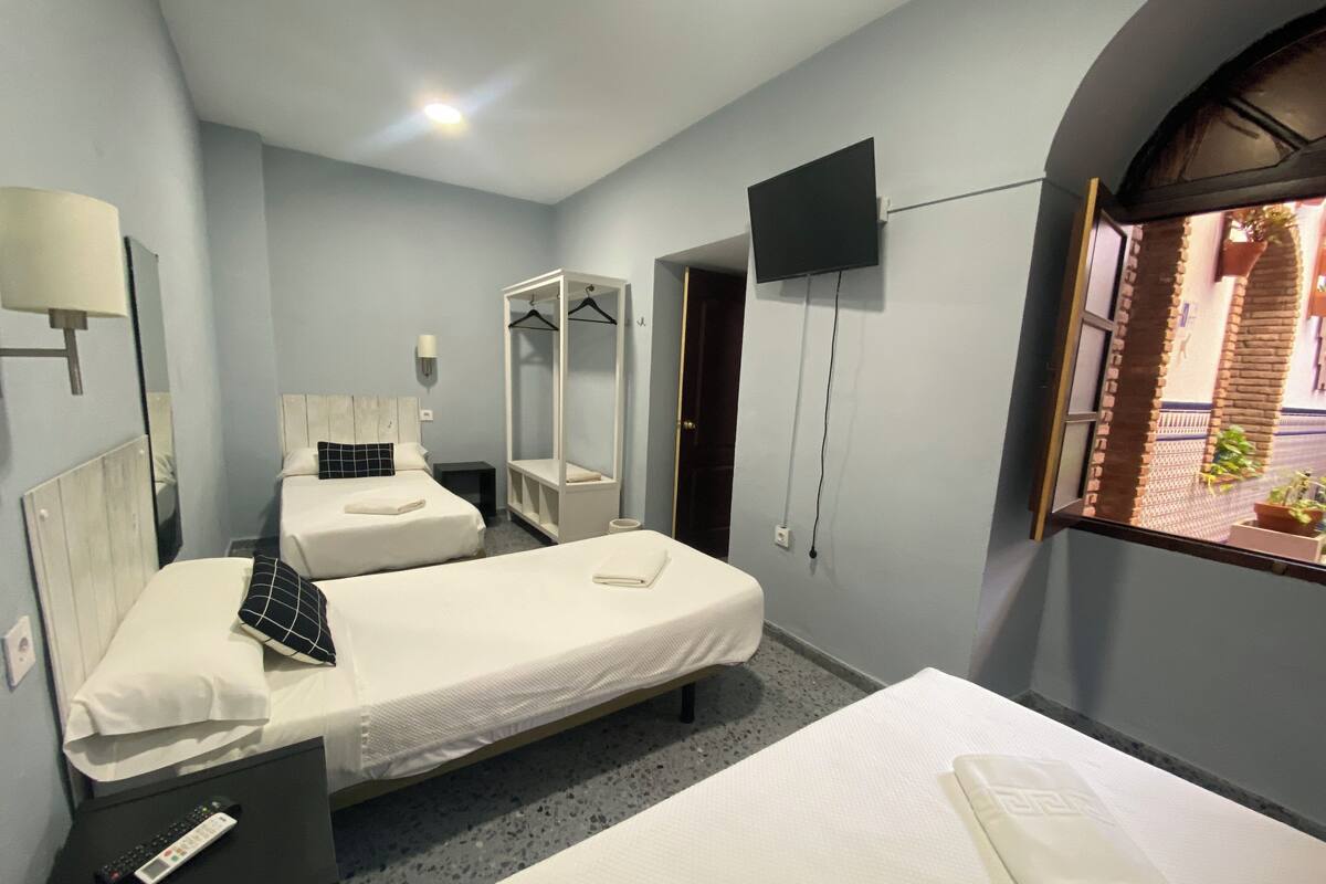 Quarto de hotel com duas camas, televisão fixada na parede, espelho e janela com vista para o exterior.