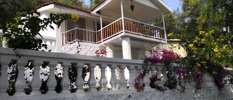 A two-story house with a balcony, white walls, and a stone wall with decorative vases.