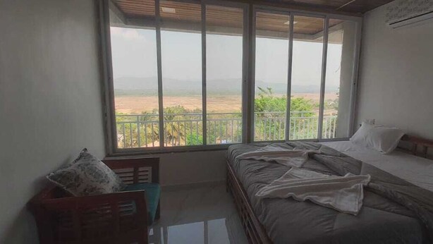 A bedroom with a large window, a bed, and a small table. - Ekdant Holiday Home (Murud)