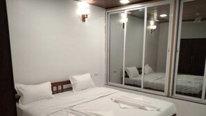 A bedroom with a large bed, white bedding, a wooden headboard, a sliding glass door, and a small wall-mounted light. - Ekdant Holiday Home (Murud)