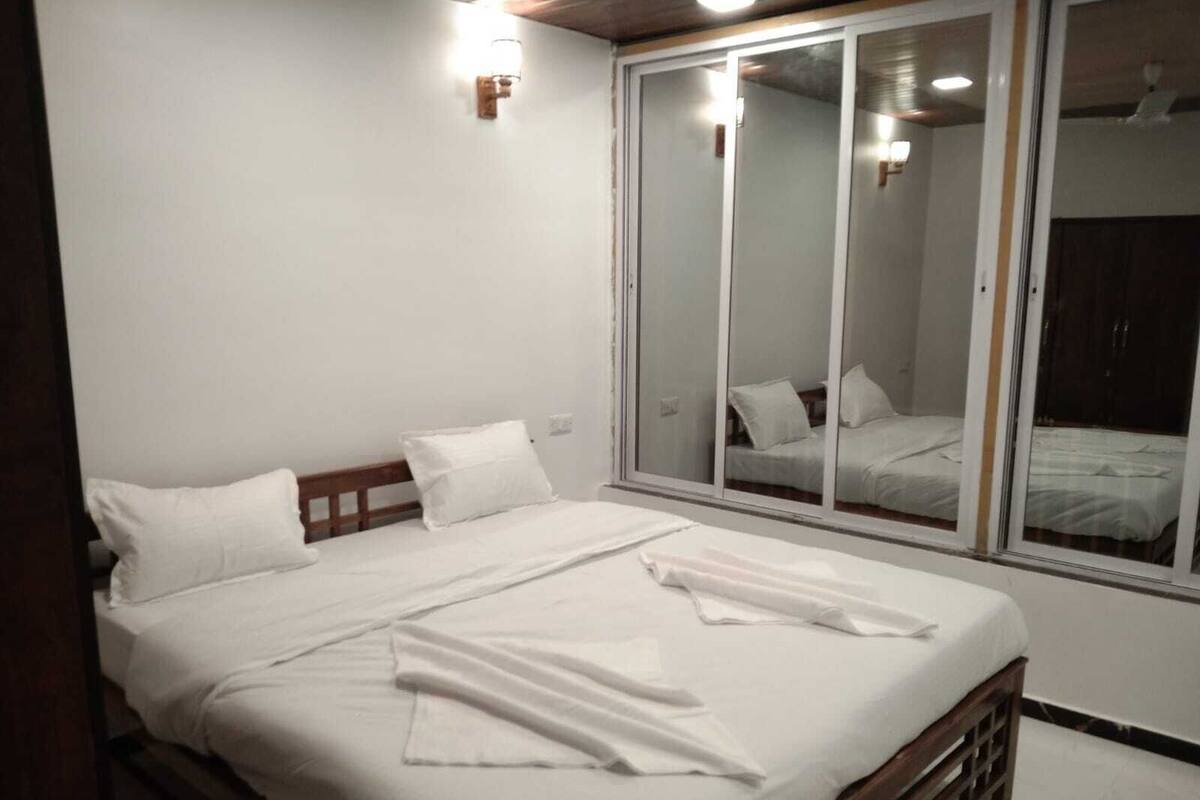A bedroom with a large bed, white bedding, a wooden headboard, a sliding glass door, and a small wall-mounted light.