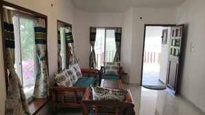 A spacious living area with a sofa set, a coffee table, and a dining table. There are curtains on the windows, and a door leading to another room. - Ekdant Holiday Home (Murud)