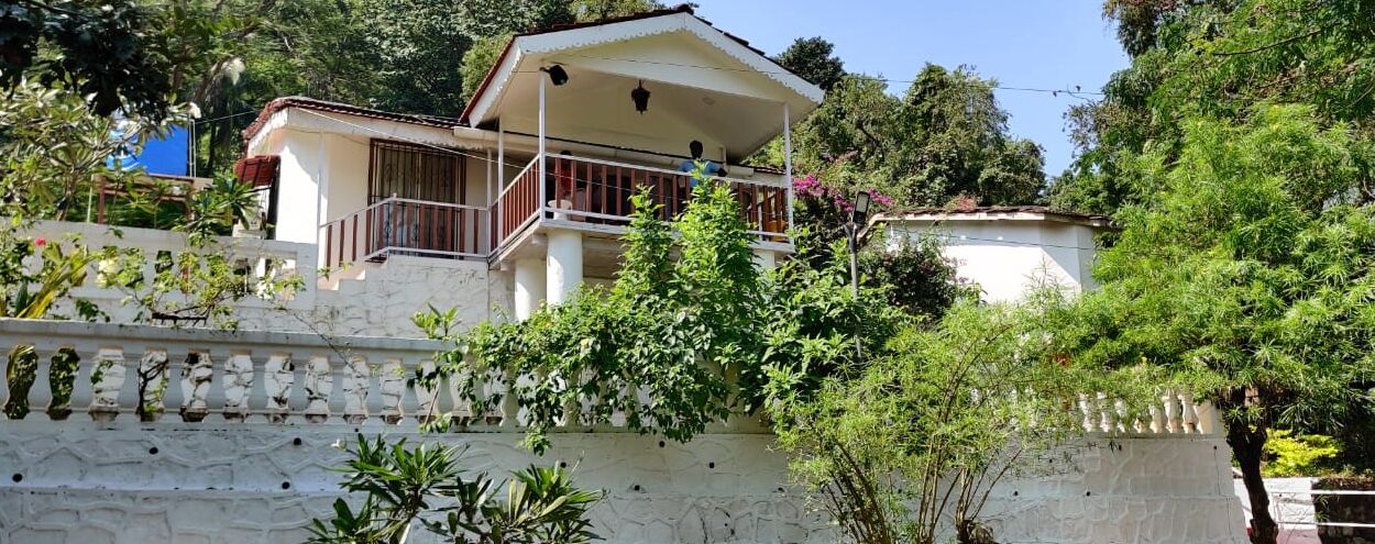 A two-story house with a balcony, surrounded by lush greenery.