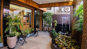 Un espai interior modern amb grans finestres, plantes en testos, zona de seients i una font.