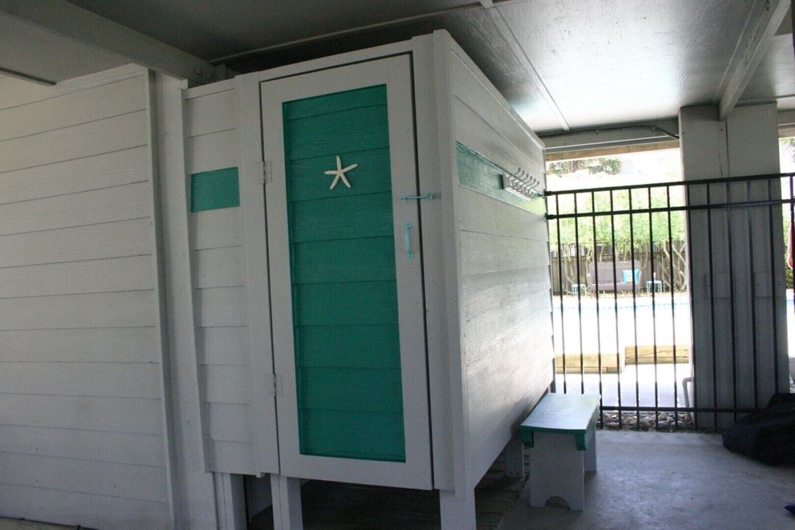 Una habitació amb un armari blanc i verd, una banca i una reixa de metall.