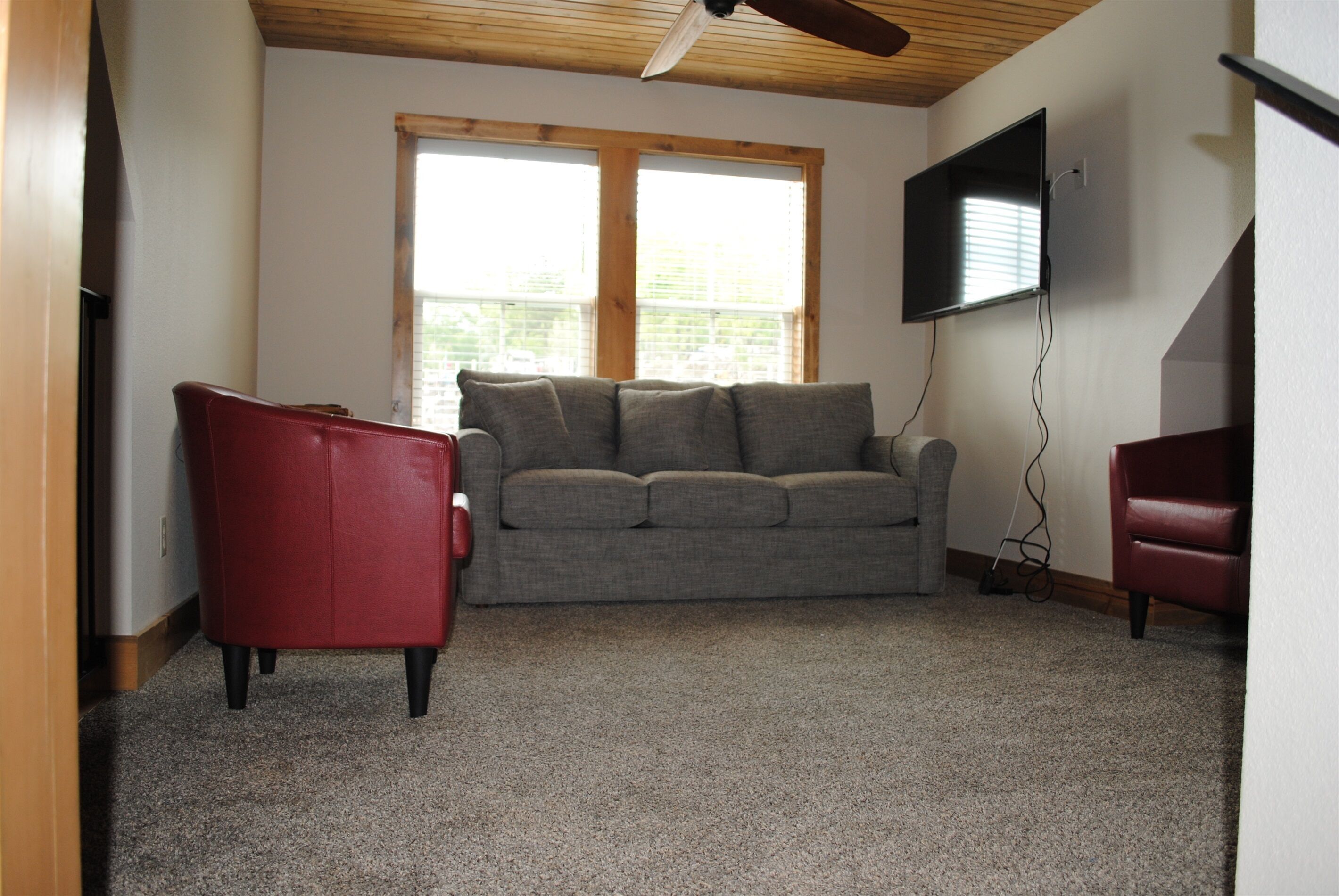 A living room with a grey sofa, a red armchair, and a television mounted on the wall.
