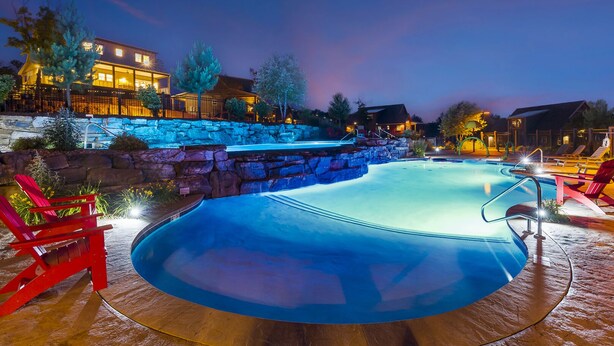 A swimming pool with a stone waterfall feature, surrounded by lounge chairs and a stone wall. - Bluff Cabin #5 -  Dual Masters, Game Room, Hot Tub, ADA access, NO Pet Cabin. (Kimberling City)