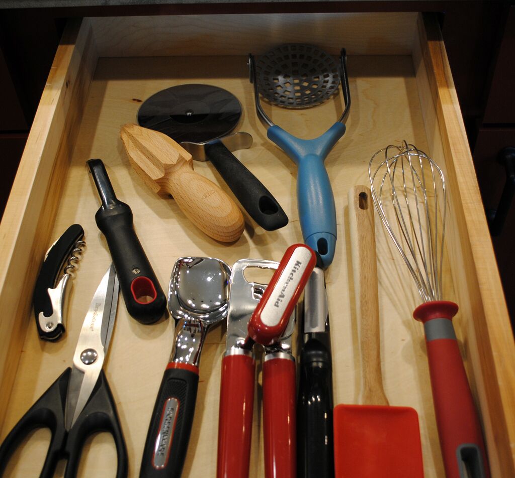 Un cajón con varios utensilios de cocina, como un rallador, batidor y un par de tijeras.