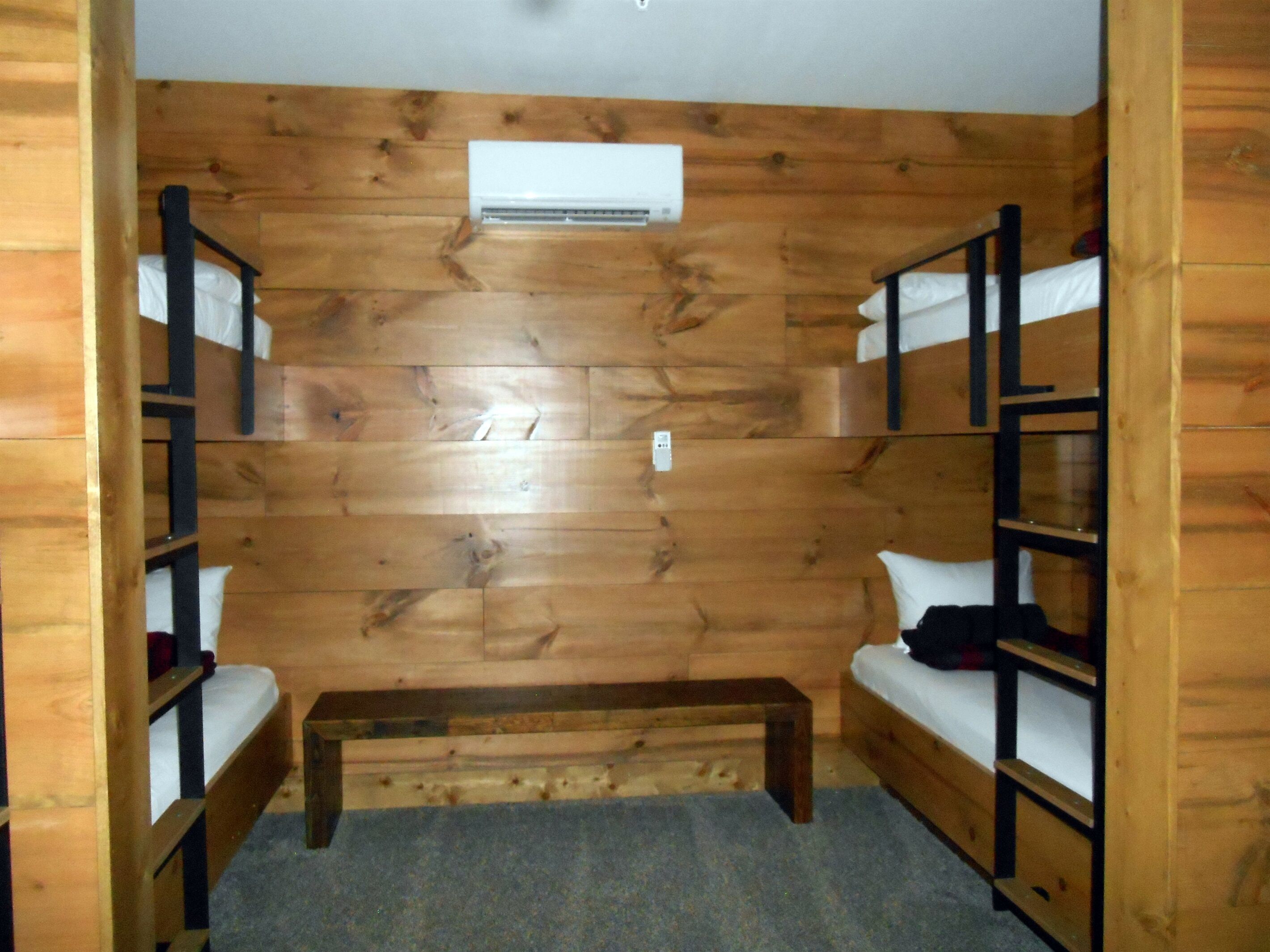 Una habitación de cabaña de madera con literas, un banco y un equipo de aire acondicionado.