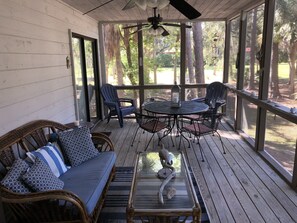 Relax in a serene outdoor space surrounded by lush greenery, featuring a round table, wicker sofa, and metal chairs.