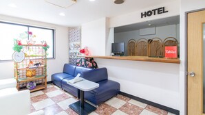 A hotel reception area with a blue sofa, a small table, a clock, a TV, and a wooden shelf with a 'Tabist' sign. - Tabist Rays Hotel Suisen (Miyazaki)