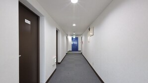 A long, narrow hallway with a carpeted floor, white walls, and a blue door at the end. - Tabist Rays Hotel Suisen (Miyazaki)