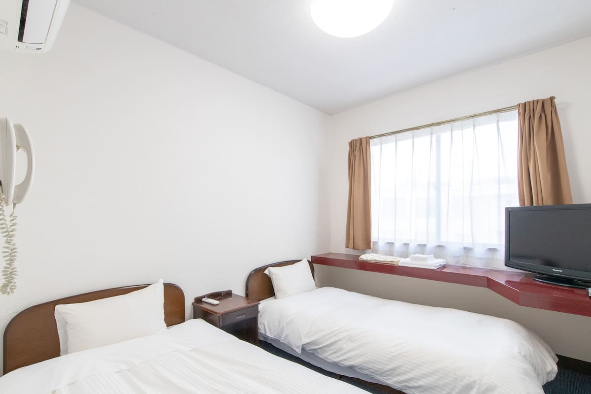 A hotel room with two beds, a TV, a phone, and a window with curtains.