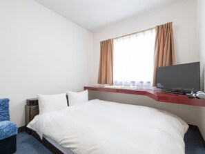 A hotel room with a bed, a TV, a desk with a computer, and a window with curtains. - Tabist Rays Hotel Suisen (Miyazaki)