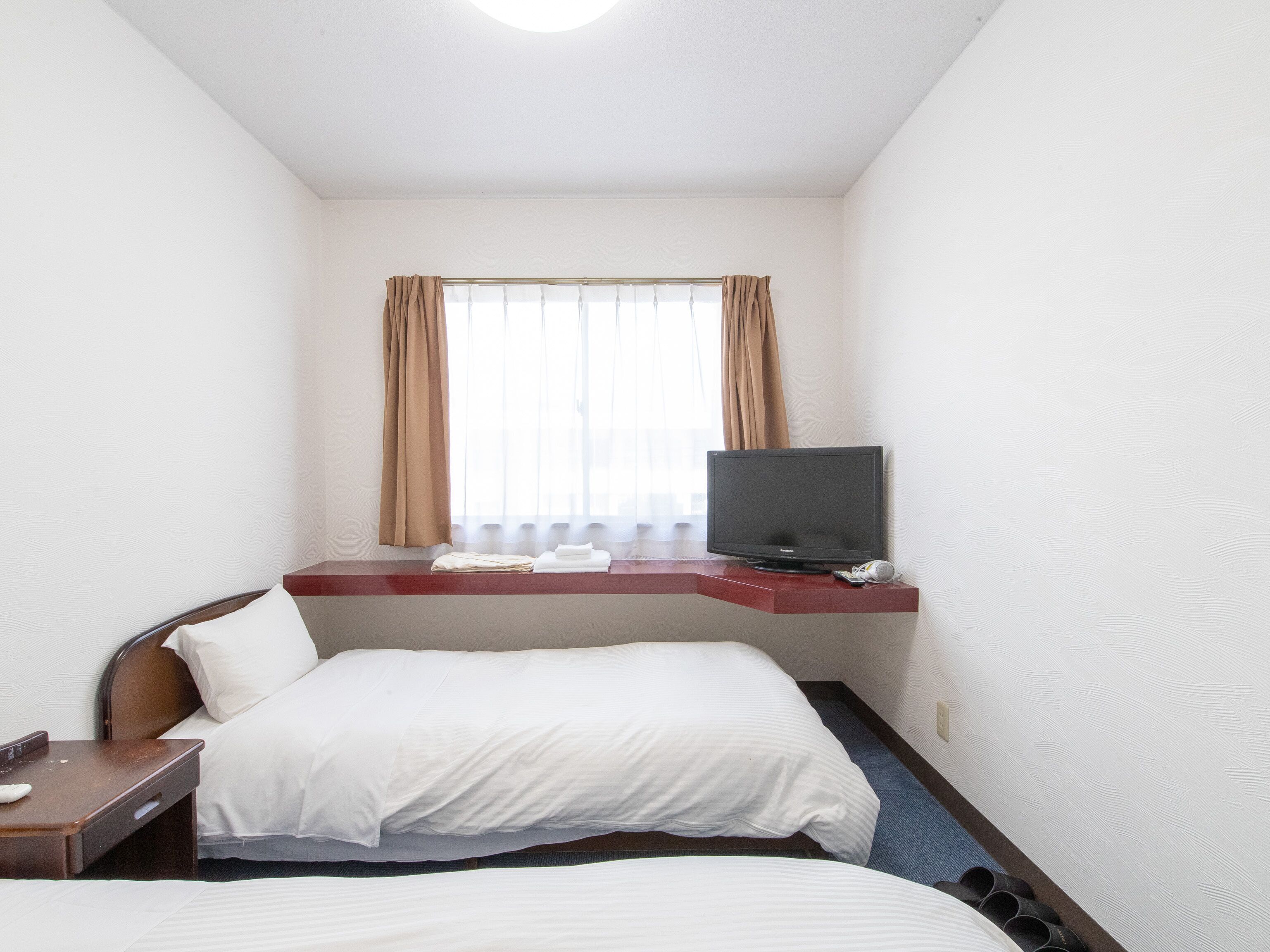 Une chambre d’hôtel avec deux lits, un téléviseur posé sur un meuble, un bureau avec une chaise et une fenêtre avec des rideaux.
