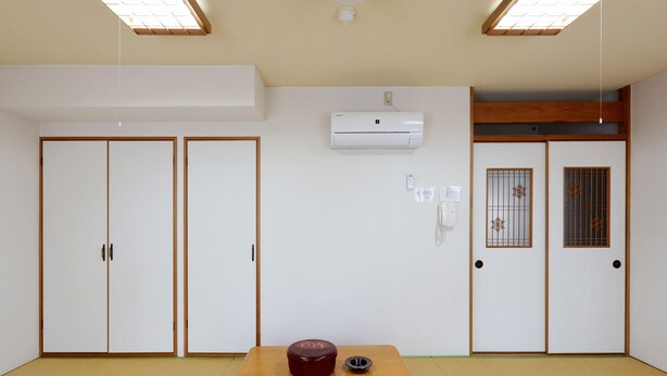 A room with tatami flooring, a wooden table with a red container, a wall-mounted air conditioner, and a sliding door with decorative patterns. - Tabist Rays Hotel Suisen (Miyazaki)