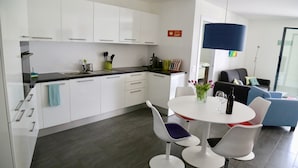 Eine moderne Küche mit weißen Schränken, einer schwarzen Arbeitsplatte und einem Essbereich mit einem weißen Tisch und zwei weißen Stühlen.
