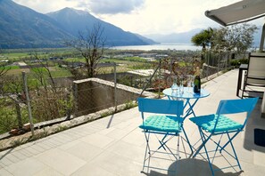 A terrace with a table and chairs overlooking a scenic valley and lake. - Beautiful Lake-view Apartment (Gordola)