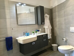 Une salle de bain moderne avec un grand miroir, un lavabo, des toilettes et un meuble de rangement.